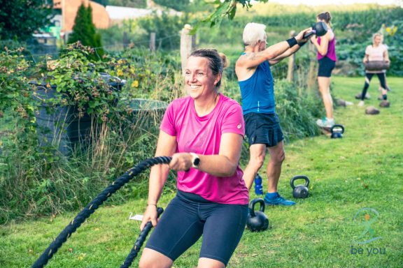 Frauen und Männer trainieren im Freien mit Seilen und Gewichten, lächelnde Sportler.