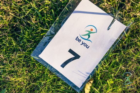 Nummer 7 auf einem Schild mit dem Logo "be you" auf grünem Gras.