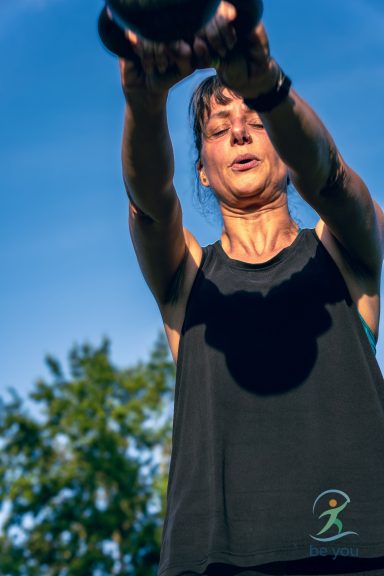 Frau hebt eine Hantel im Freien unter klarem Himmel.