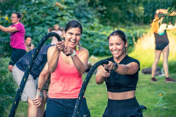 Zwei lächelnde Frauen in Sportkleidung, die mit Fitnessseilen trainieren.