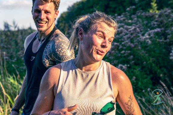 Zwei fröhliche Sportler nach dem Training, umgeben von grüner Natur.