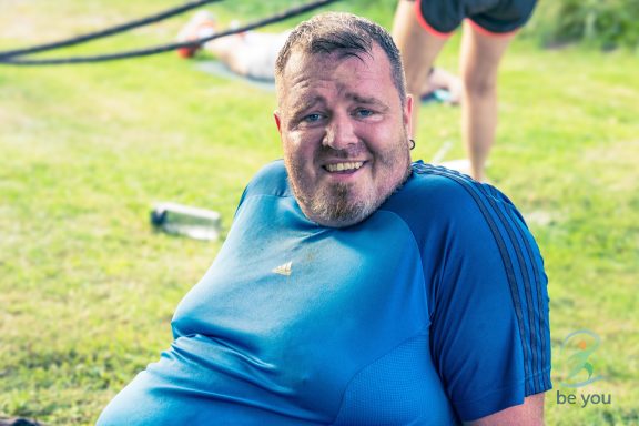 Mann in Sportkleidung sitzt im Gras und lächelt erschöpft.