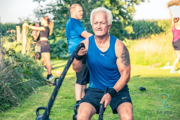 Älterer Mann im blauen Shirt trainiert mit einem Widerstandsband in der Natur.