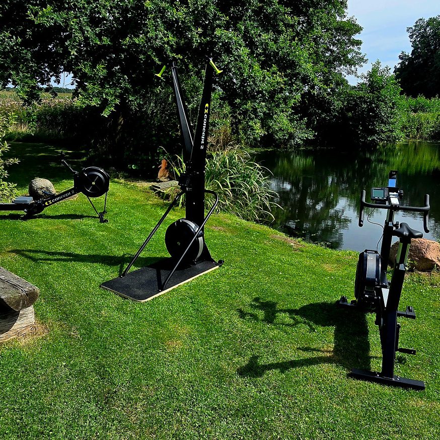 Rudergeräte und Fitnessgeräte im Garten neben einem ruhigen Teich.