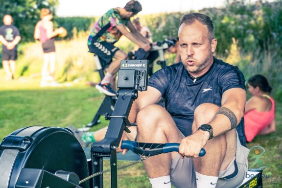 Mann beim Rudern im Freien mit weiteren Personen im Hintergrund, die aktiv sind.