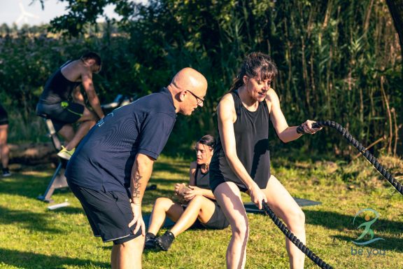 Person mit Glatze trainiert mit einer Seilübung, während andere im Hintergrund trainieren.