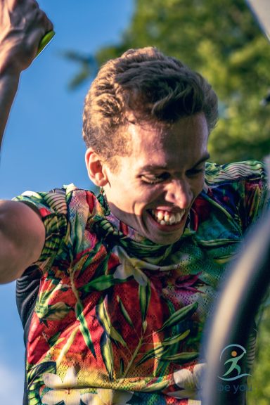 Junger Mann mit fröhlichem Ausdruck in einem bunten T-Shirt, hebt die Arme in die Luft.