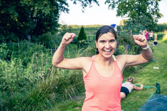 Eine fröhliche Frau in einem pinken Top hebt die Arme in Feierlaune.