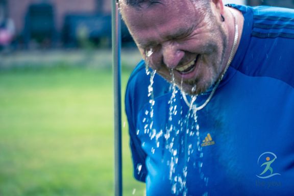 Mann lacht, während Wasser über seinen Kopf läuft, im Freien stehend.