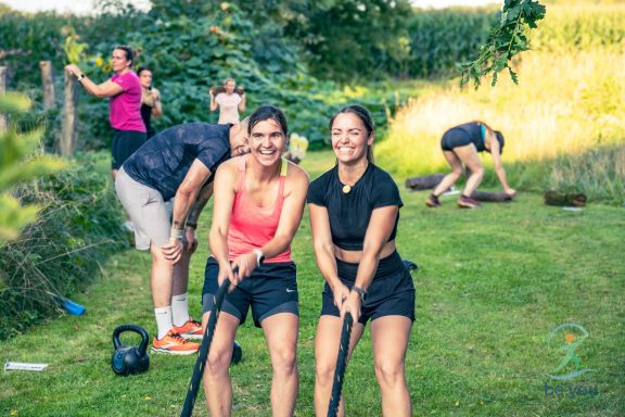 Zwei Frauen ziehen an Seilen, im Hintergrund Personen arbeiten im Garten.