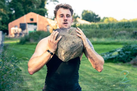 Junger Mann hebt einen großen Stein über seinem Kopf auf einem Feld.