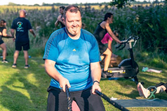 Mann mit Paddel auf dem Rasen, während andere im Hintergrund Sport treiben.