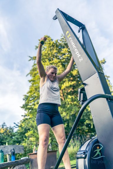 Frau trainiert an einem Rudergerät im Freien, umgeben von Bäumen und Grün.