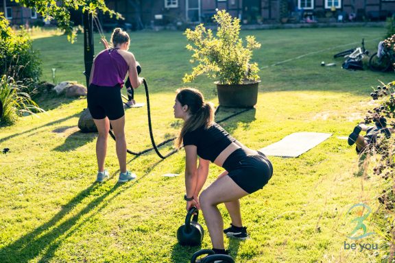 Zwei Frauen trainieren im Freien mit Kettlebell und Widerstandsbändern.