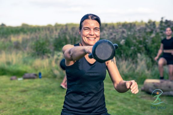 Frau in sportlicher Kleidung hebt eine Kettlebell in einer natürlichen Umgebung.